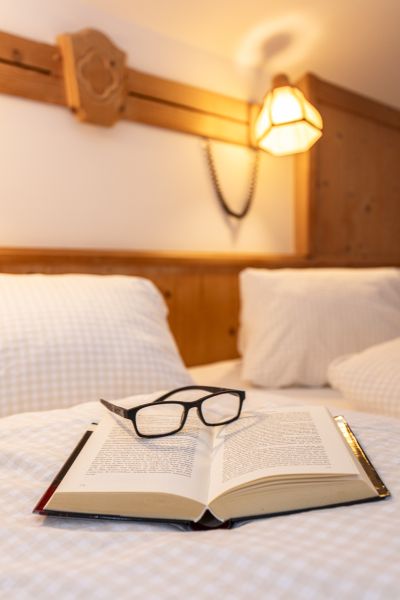 Aufgeschlagenes Buch und Brille auf dem Bett